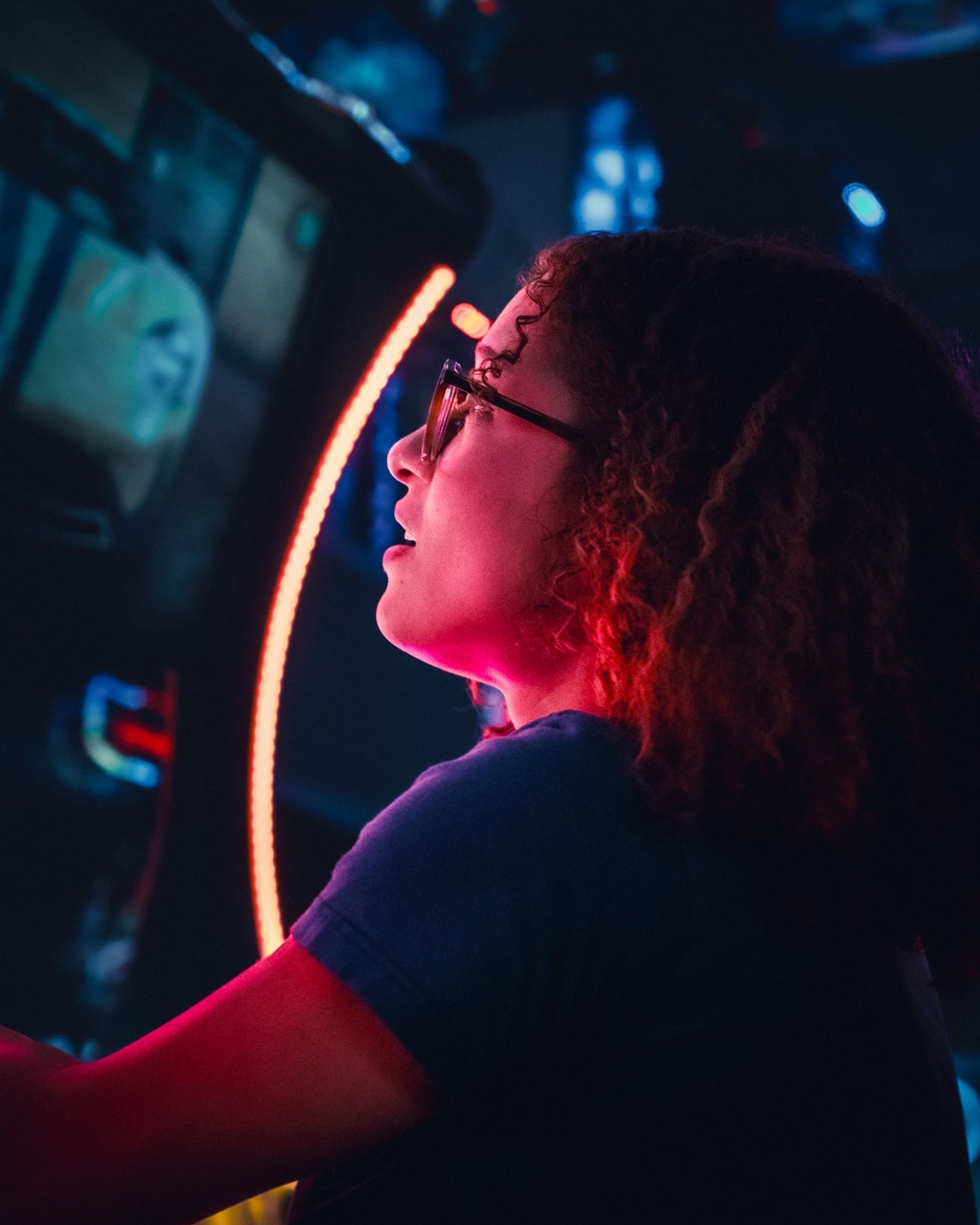 Woman with curly hair and glasses lit by red neon arcade light